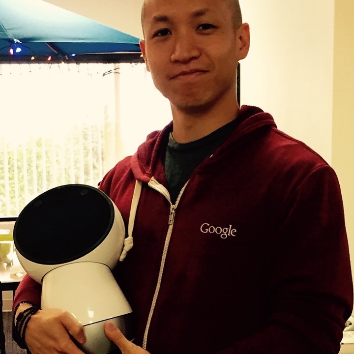 Software engineer Benedict Chen holding the white Jibo social robot, whose round black screen face and tilted three-axis body are visible in the lower left of the frame.