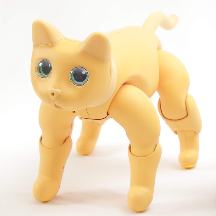 Ginger-yellow MarsCat robotic cat standing on all fours with large green eyes, photographed on a white background.