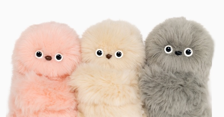 Three fluffy Mirumi robots in pink, cream, and gray sitting side by side, each with round black eyes and a tiny beak-like nose.