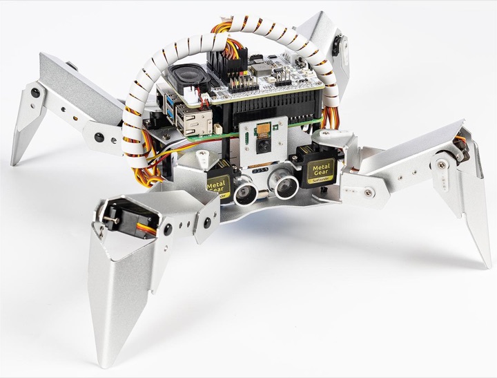 Silver aluminium PiCrawler quadruped robot with Raspberry Pi boards, camera and ultrasonic sensor on a white background.