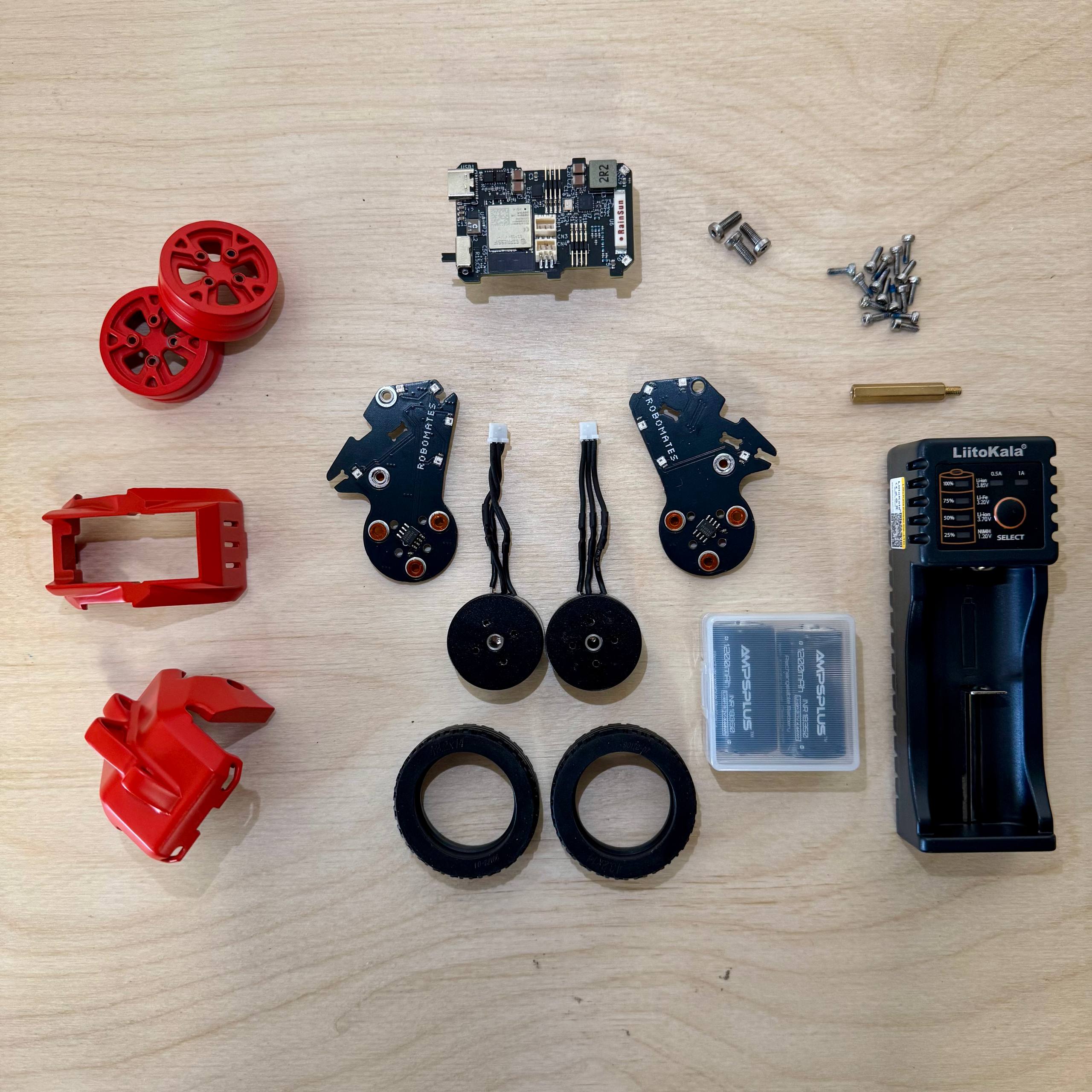 Official og:image of the product page: flat-lay of the full kit contents — red 3D-printed body parts, wheels, tyres, PCBs, motors, batteries and charger on a plywood surface.